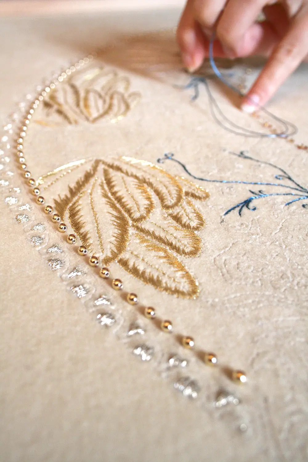 Photo issue du reportage réalisé par Luce Dupont, dans l'atelier de la brodeuse. Au premier plan, des broderies mêlant perles et fils d'or avec la main au travail en fond d'image. Photo Via tara